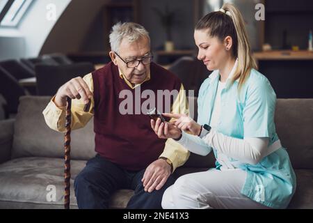 Die Pflegekraft hilft dem alten Mann zu Hause. Professionelle Gesundheitsförderung für ältere Menschen. Stockfoto