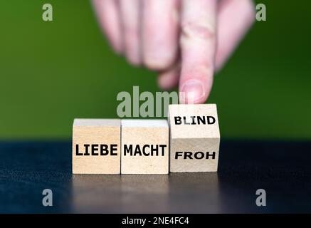 Die Hand dreht Holzwürfel und ändert den deutschen Spruch „liebe macht froh“ (Liebe macht glücklich) in „liebe macht blind“ (Liebe macht blind). Stockfoto