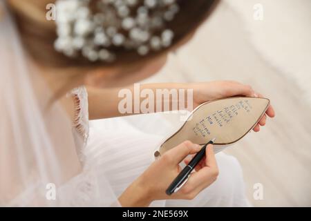 Die junge Braut schreibt die Namen ihrer Single-Freunde drinnen auf Schuhe, Nahaufnahme. Hochzeitsabergläubisch Stockfoto