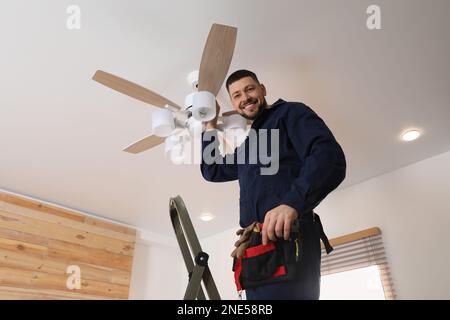 Elektriker repariert Deckenventilator mit Lampen im Innenbereich Stockfoto