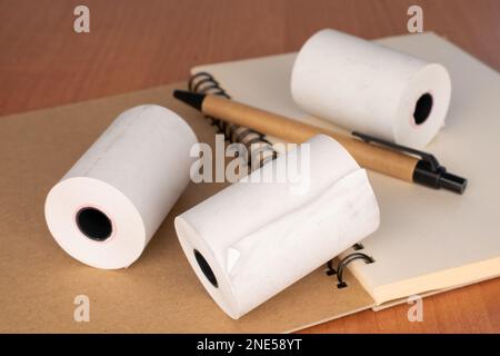 Mehrere Papierrollen Kassenband mit Notizbuch und Stift auf dem Schreibtisch, Nahaufnahme. Stockfoto