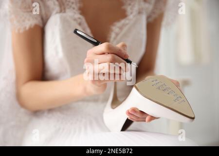 Die junge Braut schreibt die Namen ihrer Single-Freunde drinnen auf Schuhe, Nahaufnahme. Hochzeitsabergläubisch Stockfoto