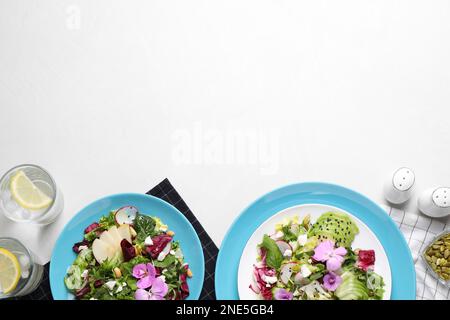 Frische Frühlingssalate mit Blumen, serviert auf einem weißen Tisch, flach liegend. Platz für Text Stockfoto