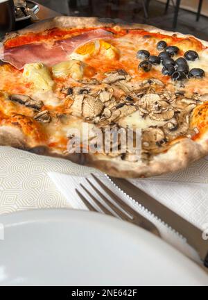 Pizza, Pizza mit seitlichem Blick mit Pilzen und Oliven auf dem Tisch mit Gabel und Messer. italienische Pizza mit Pilzen, Oliven und Speck in Italien. italienisches Essen oder C. Stockfoto