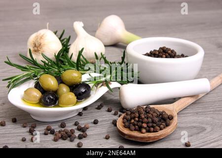 Rosmare Zweige, Knoblauch, Pfefferkörner und Oliven auf einem Teller Stockfoto