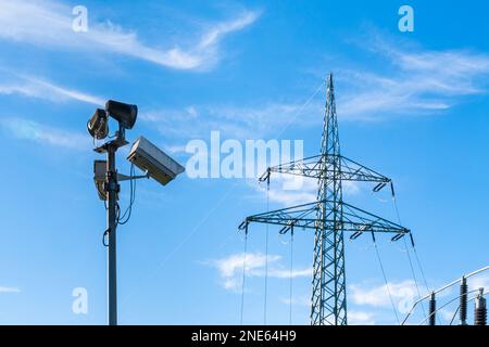 Überwachungskameras an einem Pol und ein Hochspannungsmast gegen den blauen Himmel. Stockfoto