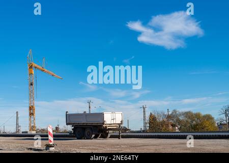 LKW-Anhänger auf der Baustelle. Im Hintergrund ein Baukran unter blauem Himmel. Stockfoto