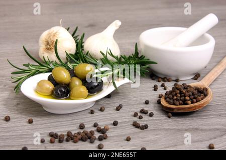Rosmare Zweige, Knoblauch, Pfefferkörner und Oliven auf einem Teller Stockfoto