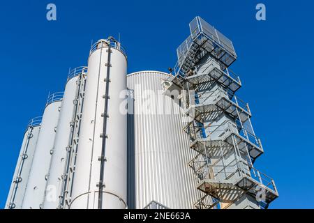 Ein zylindrischer Turm eines Industriegebäudes, der sich bis in den Himmel erstreckt. Metalltreppe mit Geländern an der Seite. Stockfoto