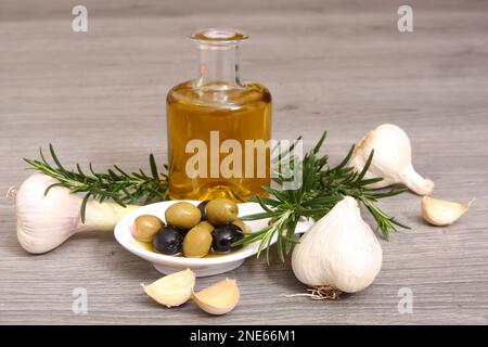 Olivenöl, Knoblauch, rosmare Zweige und Oliven auf einem Teller Stockfoto
