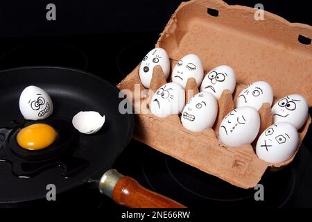 Ei in der Pfanne, Eier mit Gesichtern bemalt in einem Eierkarton Stockfoto