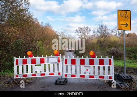 Mobile rote und weiße Kunststoffbarrieren mit orangefarbenen Lichtern blockieren den Eingang zur Baustelle. Gelbes Umleitungsschild. Stockfoto