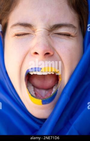 Gesicht einer verängstigten, verzweifelten jungen Frau mit offenem Mund, Lippen in gelb-blauen Farben der ukrainischen Flagge. Ein Hilferuf, um den Krieg zu beenden Stockfoto