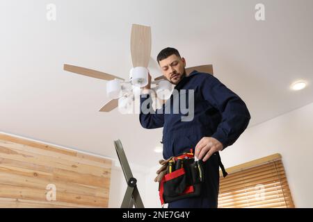 Elektriker repariert Deckenventilator mit Lampen im Innenbereich Stockfoto