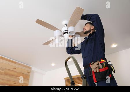 Elektriker repariert Deckenventilator mit Lampen im Innenbereich. Platz für Text Stockfoto