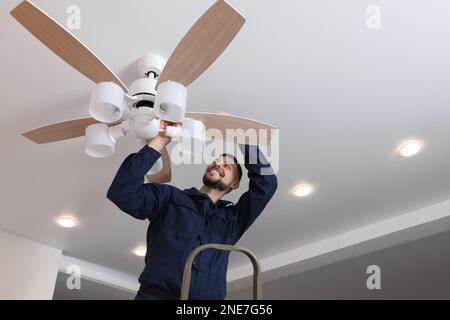 Elektriker repariert Deckenventilator mit Lampen im Innenbereich Stockfoto