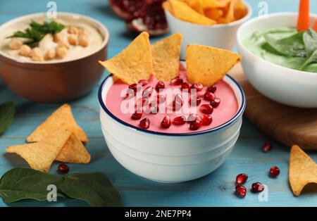 Schale mit köstlichem rosa Hummus mit Tortilla-Chips und Granatapfelsamen auf einem hellblauen Holztisch Stockfoto