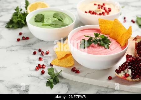 Schale mit köstlichem rosa Hummus mit Tortilla-Chips und Petersilie auf einem weißen Marmortisch Stockfoto