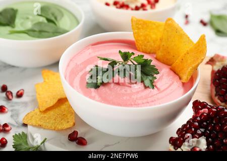 Schale mit köstlichem rosa Hummus mit Tortilla-Chips und Petersilie auf einem weißen Marmortisch Stockfoto