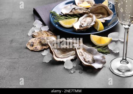 Frische Austern mit Zitrone, Rosmarin und Glas Champagner auf grauem Tisch Stockfoto