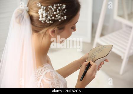 Die junge Braut schreibt die Namen ihrer Single-Freunde drinnen auf Schuhe, Nahaufnahme. Hochzeitsabergläubisch Stockfoto