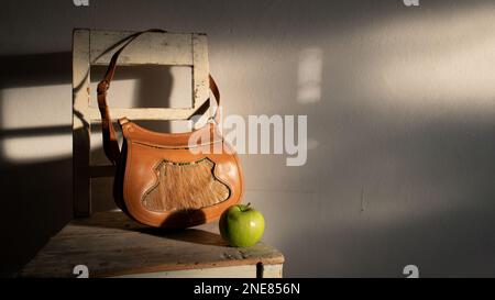 Eine Jägertasche aus echtem Leder mit einer Vorderseite, dekoriert mit Hirschhaaren und einem Apfel, die im Sonnenlicht am späten Nachmittag auf einem Stuhl liegt. Stockfoto
