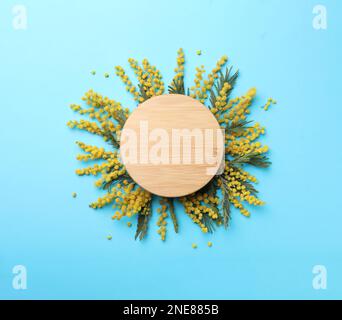 Wunderschöne Blumenzusammensetzung mit Mimosablumen und Holzbrett auf hellblauem Hintergrund, flach liegend. Platz für Text Stockfoto