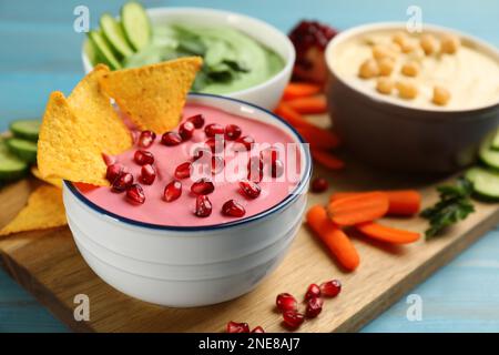 Schale mit köstlichem rosa Hummus mit Tortilla-Chips und Granatapfelsamen auf einem hellblauen Holztisch Stockfoto