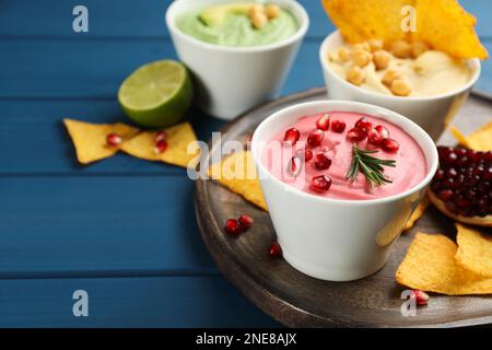 Schale mit köstlichem rosa Hummus mit Rosmarin und Granatapfelsamen auf einem blauen Holztisch. Platz für Text Stockfoto