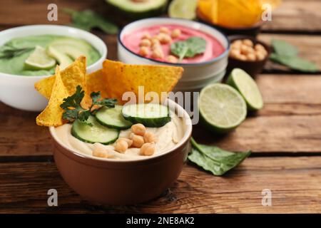 Schale mit köstlichem klassischem Hummus mit Tortilla-Chips, Gurke und Petersilie auf einem Holztisch. Platz für Text Stockfoto