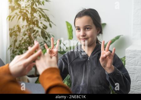 Kleines, kaukasisches Teenager-Kind Machen Sie zu Hause Artikulationsübungen mit einer fürsorglichen Mutter oder einer fürsorglichen Lehrerin. Das kleine Kind spricht Geräusche aus, spricht mit dem Lehrer oder Stockfoto