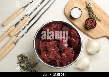 Flache Liegezusammensetzung mit Metallspießen und frischem Fleisch auf weißem Holztisch Stockfoto