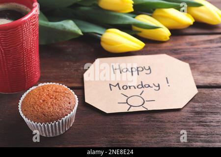 Happy Monday Nachricht, aromatischer Kaffee, Cupcake und Tulpen auf Holztisch Stockfoto