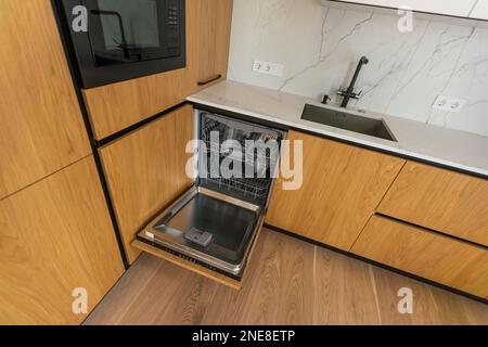 Moderne Küche mit leerer Einbauspülmaschine mit geöffneter Tür, Edelstahl-Spülbecken und Leitungswasser, schwarzem Induktionskochfeld, Herd Stockfoto