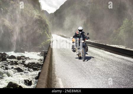 Motorrad fährt schnell auf der Wet Canyon Valley Road und Brücke über den Fluss. Motobiker Journey in Norwegen. Stockfoto