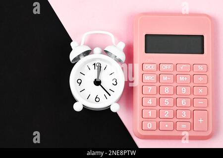 Taschenrechner und Wecker auf pinkfarbenem und schwarzem Hintergrund. Draufsicht. Flach verlegt Stockfoto