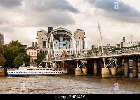 Blick vom Südufer der Thames River of Charing Cross Station, der Hungerford Eisenbahnbrücke und der angrenzenden Golden Jubilee Fußbrücke. Stockfoto