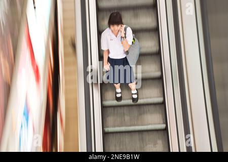 <ngko, Thailand - May 12, 2009: student on the moving staircase in school dress using the mobile Stockfoto