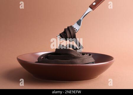 Gabel mit Schnürsenkel über dem Teller auf braunem Hintergrund Stockfoto