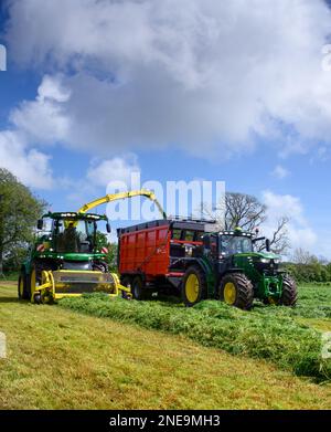 Selbstfahrender Feldhäcksler von John Deere, der einen von einem Traktor von John Deere gezogenen Anhänger mit Gras für eine Silageklammer auf einem Milchviehbetrieb in Dumfries, Großbritannien, füllt. Stockfoto