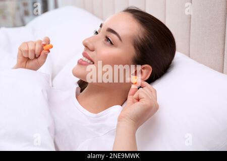 Junge Frau, die Schaumstoff-Ohrstöpsel ins Bett einsetzt Stockfoto