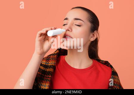 Frau, die Nasenspray auf pfirsichfarbenem Hintergrund verwendet Stockfoto