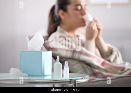 Nasensprayflaschen, Servietten und verschwommenes Bild einer kranken Frau im Hintergrund Stockfoto