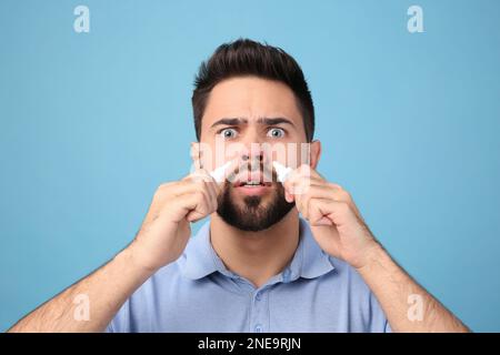 Mann mit Nasensprays auf hellblauem Hintergrund Stockfoto