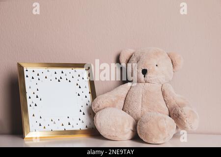 Leerer Bilderrahmen und Teddybär auf weißem Tisch nahe der grauen Wand. Raum für Design Stockfoto