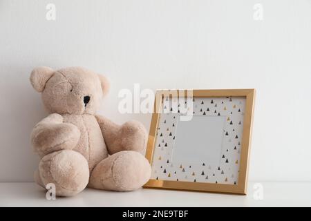 Leerer Bilderrahmen und Teddybär auf dem Tisch nahe der weißen Wand. Raum für Design Stockfoto