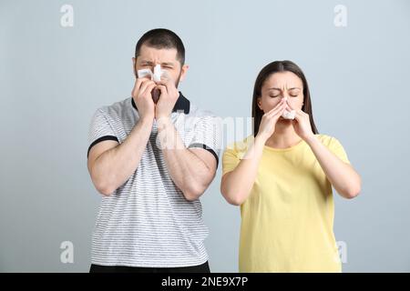 Mann und Frau mit Gewebe mit laufender Nase auf hellgrauem Hintergrund Stockfoto