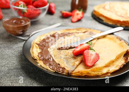 Köstliche dünne Pfannkuchen mit Schokoladenpaste und Erdbeeren auf einem grauen Tisch Stockfoto