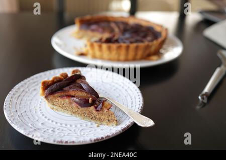 Ein Stück Pflaumen- und Mandeltörtchen mit Frangipan auf einem weißen Teller. Selektiver Fokus. Stockfoto