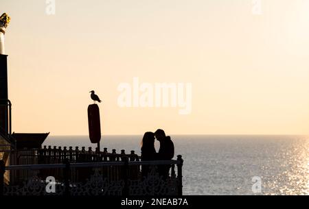 Young love on Brighton Palace Pier mit Blick auf den Sonnenuntergang, Sussex, England Großbritannien Stockfoto